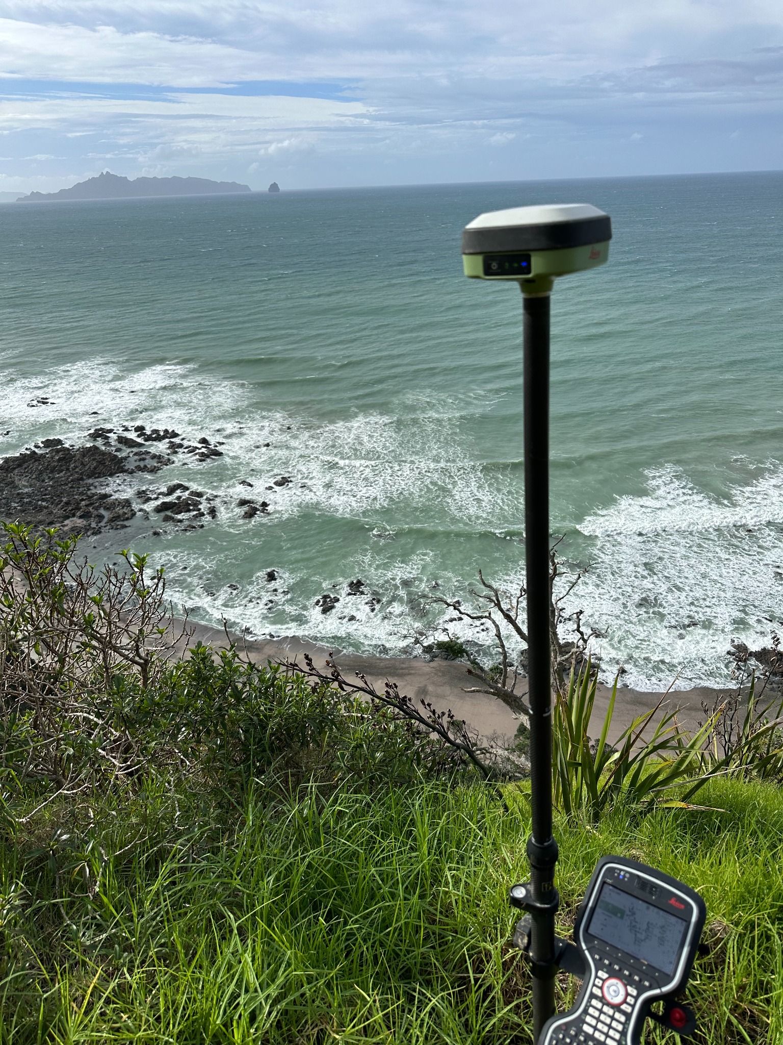 GNSS survey receiver and field controller overlooking the Mangawhai coastline and offshore islands